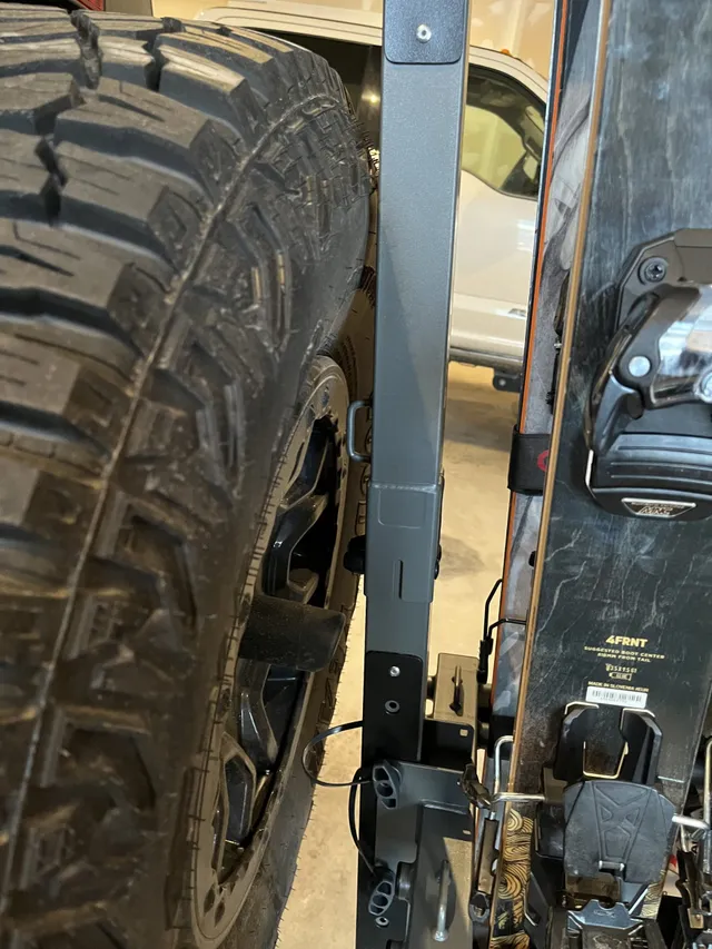 Close-up of the rack's mounting arm beside the Bronco's tire and skis