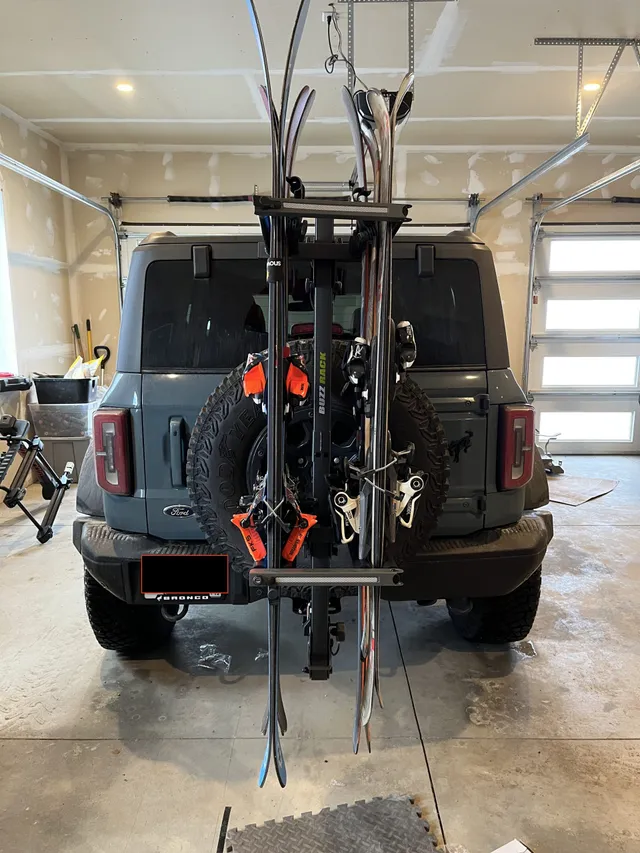 Skis and gear loaded on the hitch rack on the back of a Ford Bronco in a garage