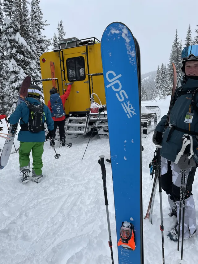 Skiers and a blue ski beside the yellow snowcat