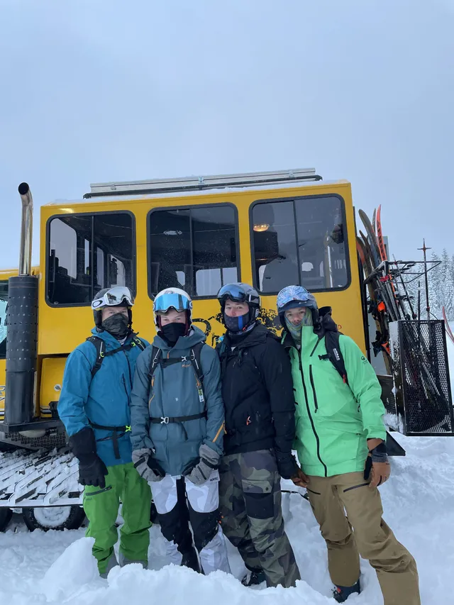 Four skiers posing in front of the yellow snowcat