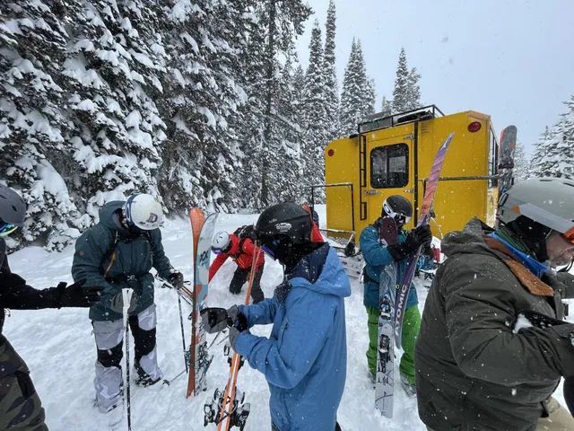 Skiers loading skis and gear beside the yellow snowcat