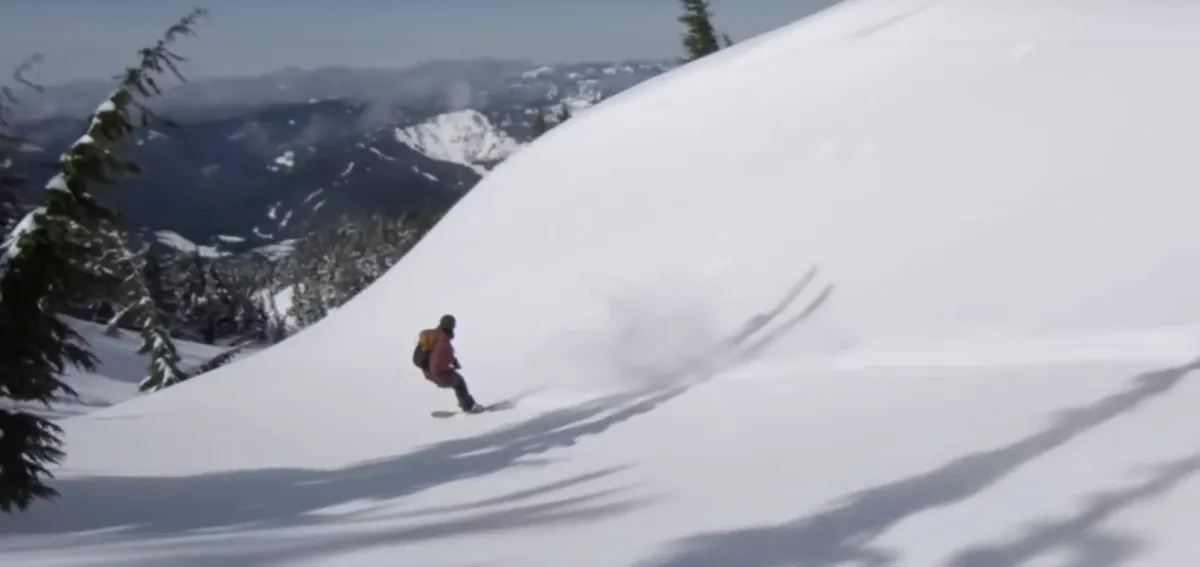 Skier in a red jacket carving through powder on a big open slope