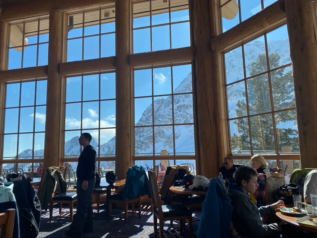 Dining room with tall log-framed windows looking out at snowy peaks